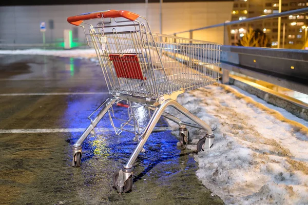 An abandoned shopping cart standing on the street near supermarket in the winter.