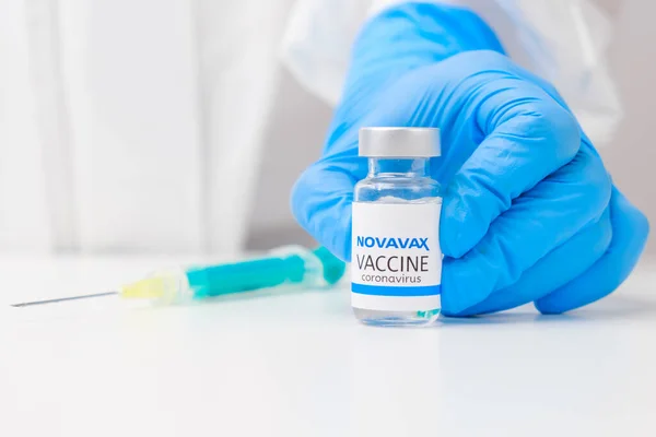 Novavax vaccin mot coronavirus och spruta för injektion på bordet och vårdpersonal hand i gummihandskar och skyddsdräkt på bakgrunden, Mars 2021, San Francisco, USA — Stockfoto