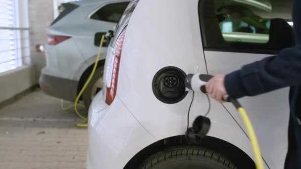 Деловая женщина вставляет зарядное устройство в электромобиль в точке зарядки на парковке на фоне другого зарядного автомобиля. — стоковое видео
