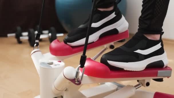 Vista frontal de los pies de las mujeres en la máquina de pasos haciendo ejercicio en casa — Vídeos de Stock