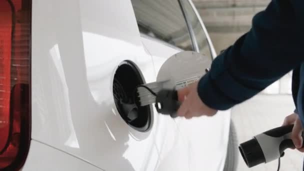 Mujer de negocios insertando un cargador en el coche eléctrico en el punto de carga en el aparcamiento — Vídeos de Stock