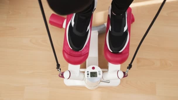 Вид зверху на жіночі ноги роблять вправи на червоному сходинці в чорних кросівках вдома на дерев'яній підлозі — стокове відео
