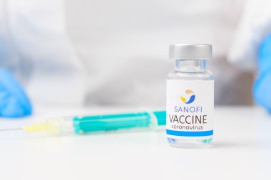 Koronavirüse karşı Sanofi aşısı ve enjeksiyon için şırınga masada ve sağlık çalışanı elinde kauçuk eldiven ve koruyucu giysi ile arka planda, Mart 2021, San Francisco, ABD