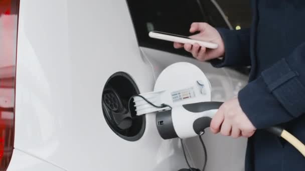 Close up woman hand plugging power cord to an electric car and paying using her smartphone. — Stock Video