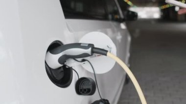 Kapalı kadın eli akıllı telefonunu EV arabasının kilidini açmak ve elektrik kablosunu elektrikli bir arabaya bağlamak için kullanır.. 