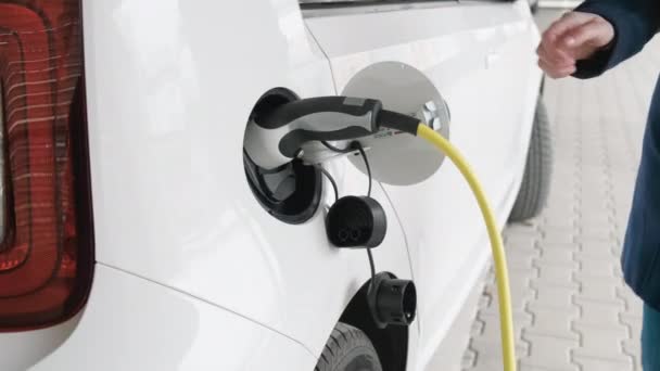 Frau öffnet Auto und koppelt Kabel von Elektroauto ab Laden eines Elektroautos oder Elektrofahrzeugs. — Stockvideo