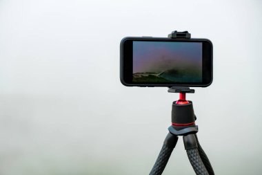 Tripodun üzerindeki akıllı telefon fotoğraf çekiyor. Dağlarda hareket eden bulutların görüntüsünü ya da zaman atlamasını yakalamak. Günlük kaydı için aygıt 