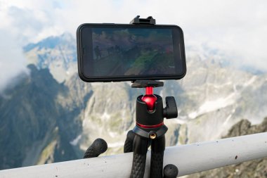 Tripodun üzerindeki akıllı telefon fotoğraf çekiyor. Dağlarda hareket eden bulutların görüntüsünü ya da zaman atlamasını yakalamak. Günlük kaydı için aygıt 