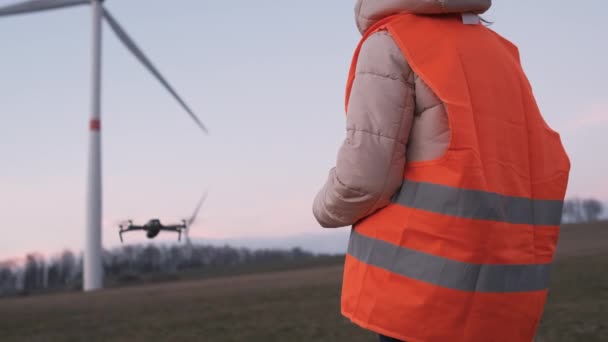 Ingeniera femenina utiliza un dron para comprobar el rendimiento de un sistema de turbina salvaje o molino de viento al atardecer. — Vídeos de Stock