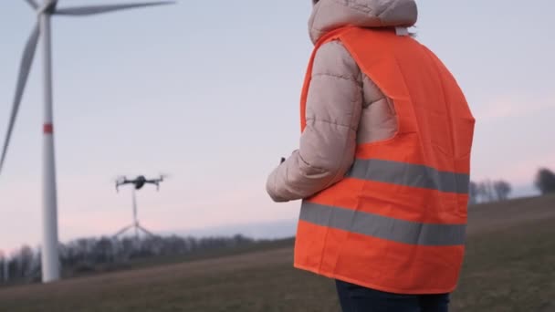 Kobieta inżynier używa drona do sprawdzenia wydajności systemu dzikiej turbiny lub wiatraka o zachodzie słońca.. — Wideo stockowe