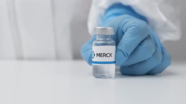 Флакон Merck с лекарством, поставленным на стол медицинским работником в резиновых перчатках и костюме СИЗ, май 2021 года, Сан-Франциско, США — стоковое видео