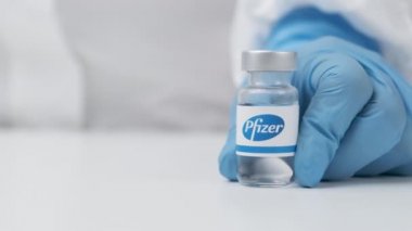 Sağlık çalışanı tarafından masaya konan plastik eldiven ve PPE takım elbiseli Pfizer şişesi, Mayıs 2021, San Francisco, ABD