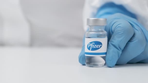 Флакон Pfizer с лекарством, поставленным на стол медицинским работником в резиновых перчатках и костюме СИЗ, май 2021 года, Сан-Франциско, США — стоковое видео