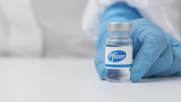 Флакон Pfizer с лекарством, поставленным на стол медицинским работником в резиновых перчатках и костюме СИЗ, май 2021 года, Сан-Франциско, США — стоковое видео