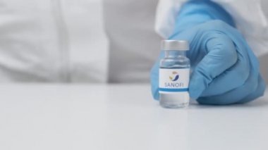Sağlık görevlileri tarafından masaya konulan plastik eldiven ve PPE takım elbiseli Sanofi şişesi, Mayıs 2021, San Francisco, ABD