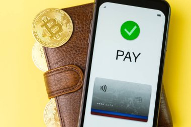 Cüzdandaki akıllı telefon ekranına ödeme başvurusu ve sarı arka planda bitcoin 'ler.