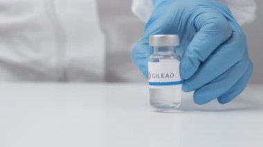 Sağlık çalışanı tarafından masaya konan plastik eldiven ve PPE takım elbiseli Gilead şişesi, Mayıs 2021, San Francisco, ABD