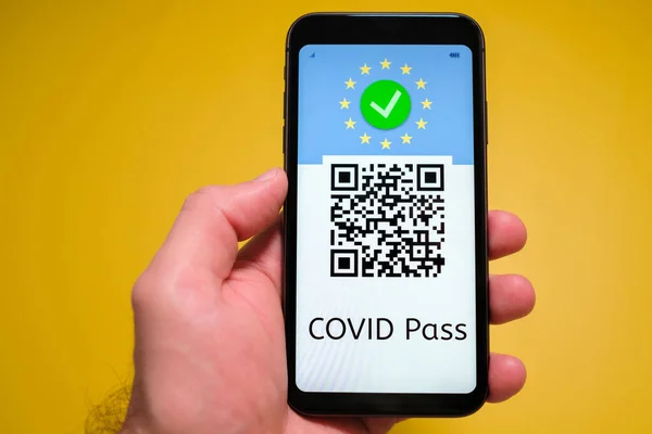 Covid pass with QR code on the screen in smartphone in mans hand on the yellow background, May 2021, San Francisco, USA.
