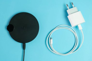 Siyah kablosuz şarj cihazı beyaz bir USB 'ye çarpıyor. Mavi arka planda bir kablo.
