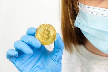 Kadın eli lastik eldiven ve koruyucu yüz maskesi içinde altın bitcoin para taşıyor..