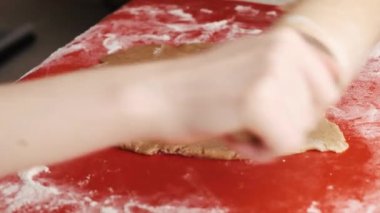 Kadın hamuru kırmızı silikon bir fırın paspasının üstünde merdaneyle yuvarlıyor.