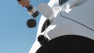 Kadın elinin alt görünümü mavi gökyüzünün arka planında elektrik veya EV araba yüklemek için güç kablosu arzı ekler