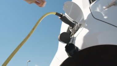 Mavi gökyüzü, Mart 2021, Prag, Çek Cumhuriyeti 'nin arka planında elektrik veya EV otomobilini şarj etmek için elektrik kablolarını kesen kadının alt görünümü.