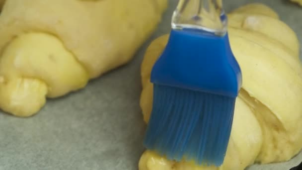 Zbliżyć rozprzestrzenianie żółtka jaj na włoskich lub francuskich rogalików z silikonową szczotką do układania na papierze piekarniczym. Ciasto domowe. — Wideo stockowe