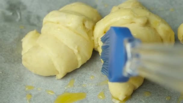 Escovar a gema de ovo nos croissants com uma escova de silicone. Pastelaria caseira. — Vídeo de Stock