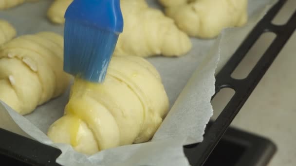 Close-up aanbrengen van een eigeel met siliconen borstel op Italiaanse croissants. bladerdeeg — Stockvideo