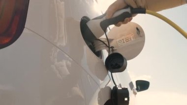 Kadın elinin alt görünümü, elektrik veya EV otomobilleri gün ışığında şarj etmek için güç kablosu arzı yerleştirir