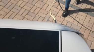 Arabanın çatısından bak. Kadın eli elektrik kablosunu koparıyor. Elektrikli araba şarj ediliyor.