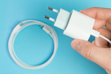 Yıldırımlı beyaz akıllı telefon şarj kablosu yüksek hızlı USB tip C konnektörü ve mavi arka planda insan eli ile adaptör..