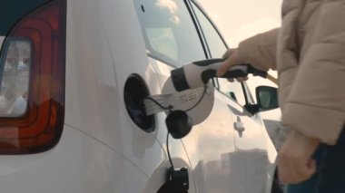 Kapalı kadın eli, güneşli bir günde şarj etmek için arabaya bir elektrik prizi yerleştirir..
