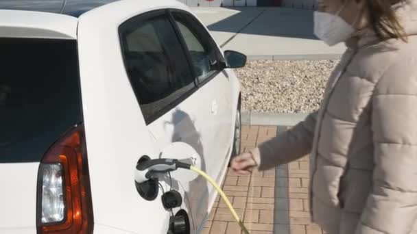 Žena v ochranné masce obličeje nebo respirátoru odpojení elektrického vozidla od nabíjení na ulici — Stock video