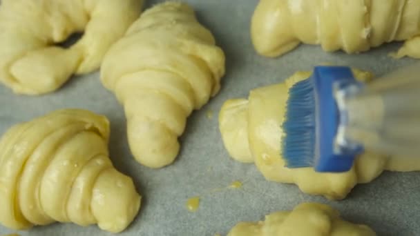 Escovar a gema de ovo nos croissants com uma escova de silicone. Pastelaria caseira. — Vídeo de Stock