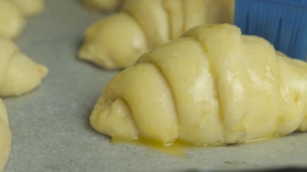 Cepillar la yema de huevo en los croissants con un cepillo de silicona. Pastelería casera. — Vídeo de stock