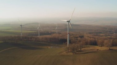 Gün batımında rüzgar türbini olan bir çiftliğin panoramik görüntüsü. Rüzgar türbinleri elektrik üretiyor..
