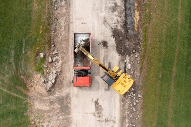 Kazıcı tarlanın yanında kazı alanı kazıyor ve kamyona yüklüyor. 