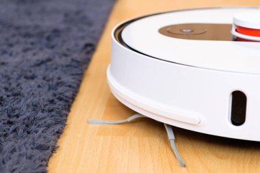 Robot elektrikli süpürge halının yanındaki ahşap zemini temizliyor. Oda servisi akıllı teknoloji.