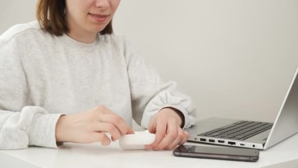 Kobieta wkłada słuchawki bezprzewodowe do ucha i pisze na notesie. — Wideo stockowe