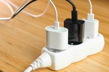 Tahta masanın üzerinde bağlı beyaz ve siyah elektrik prizleri olan elektrik uzatma şeridi. Elektrik prizleri için şarjlı akıllı telefonlar.