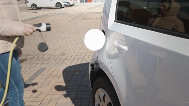 Mulher chegando ao veículo elétrico e conectando o cabo de alimentação para carregar na rua no ponto de carregamento — Vídeo de Stock