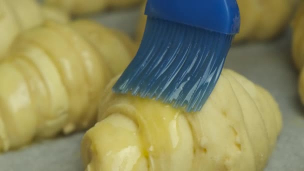 Close-up verspreiding van eigeel op Italiaanse of Franse croissants met siliconen borstel op bakpapier. Zelfgemaakt gebak. — Stockvideo