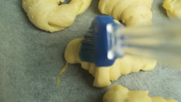 Close-up verspreiding van eigeel op Italiaanse of Franse croissants met siliconen borstel op bakpapier. Zelfgemaakt gebak. — Stockvideo