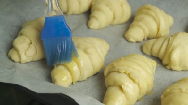 Borstel de eidooier op de croissants met een siliconen kookborstel. Zelfgemaakt gebak. — Stockvideo