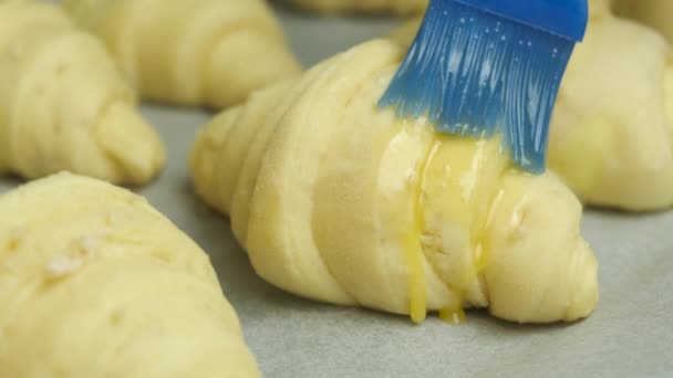 Escovar a gema de ovo nos croissants com uma escova de silicone. Pastelaria caseira. — Vídeo de Stock