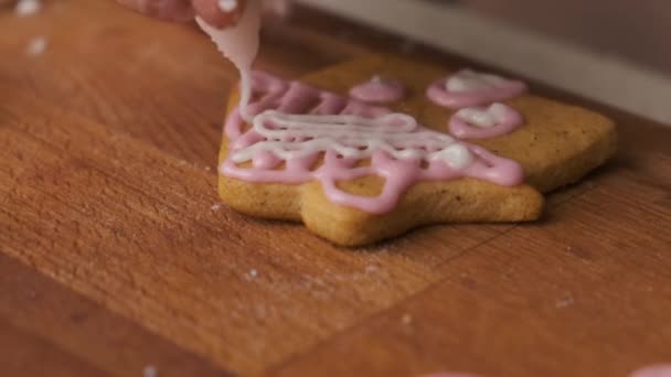 Eine Frau verziert einen Lebkuchen in Form eines Hauses auf dem Holztisch mit Zuckerguss. Weihnachtstradition. — Stockvideo