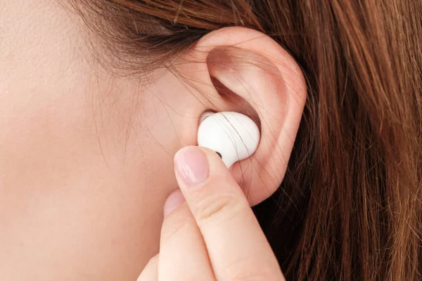 Mujer inserta auriculares inalámbricos en el oído. — Foto de Stock