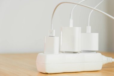 Tahta masanın üzerinde bağlı beyaz elektrik prizleri olan elektrik uzatma şeridi. Elektrik prizleri için şarj aletleri şarj ediliyor.